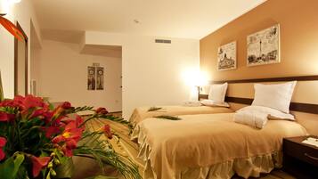 Habitación de hotel con dos camas, una mesita de noche, un espejo, un reloj de pared y un arreglo floral.