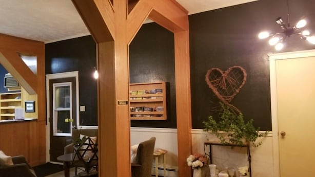 A room with a wooden ceiling, a heart-shaped wall decoration, a small table with a plant, and a door. - Silverwood Inn & Suites (Fredericton)