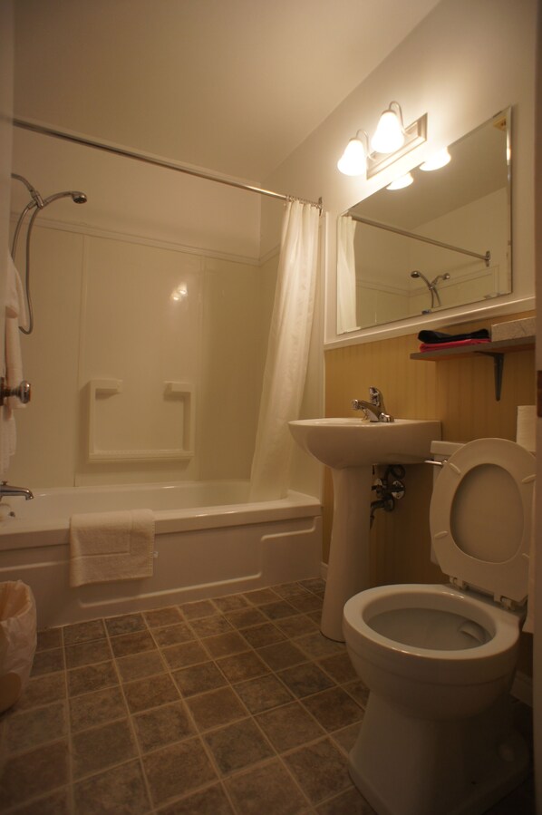 A bathroom with a bathtub, toilet, sink, and shower. - Silverwood Inn & Suites (Fredericton)