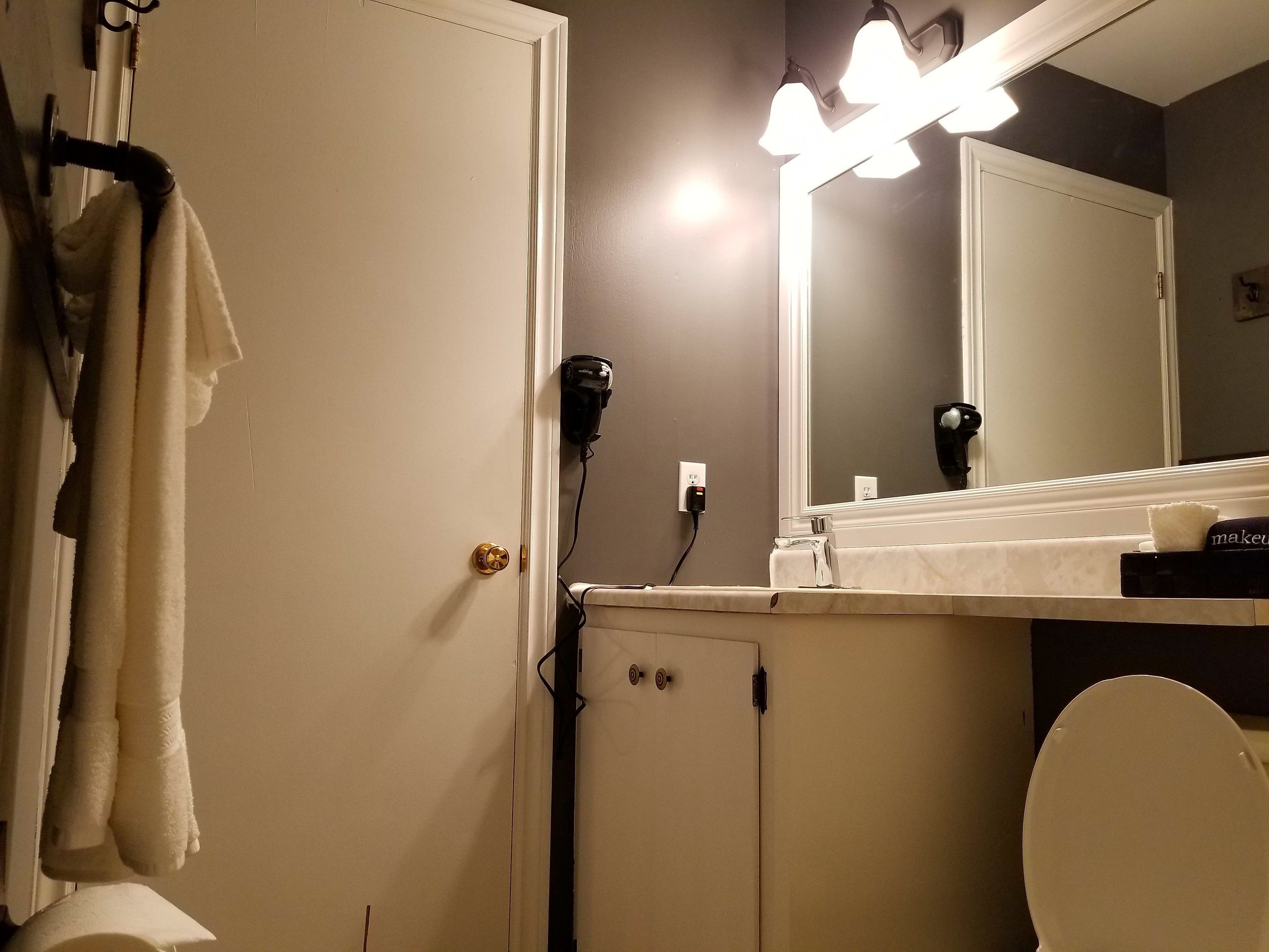 A bathroom with a white door, a towel rack, a hairdryer, a mirror, and a toilet.