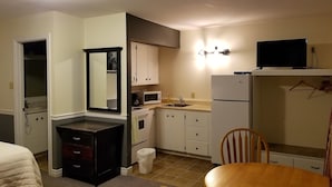 A compact kitchen with a microwave, stove, sink, and a refrigerator. There is a dining table with chairs and a mirror above the dresser. - Silverwood Inn & Suites (Fredericton)