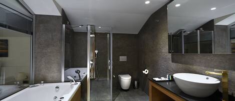 Un baño moderno con ducha envuelta en vidrio, una bañera independiente y un lavamanos grande con grifo dorado.