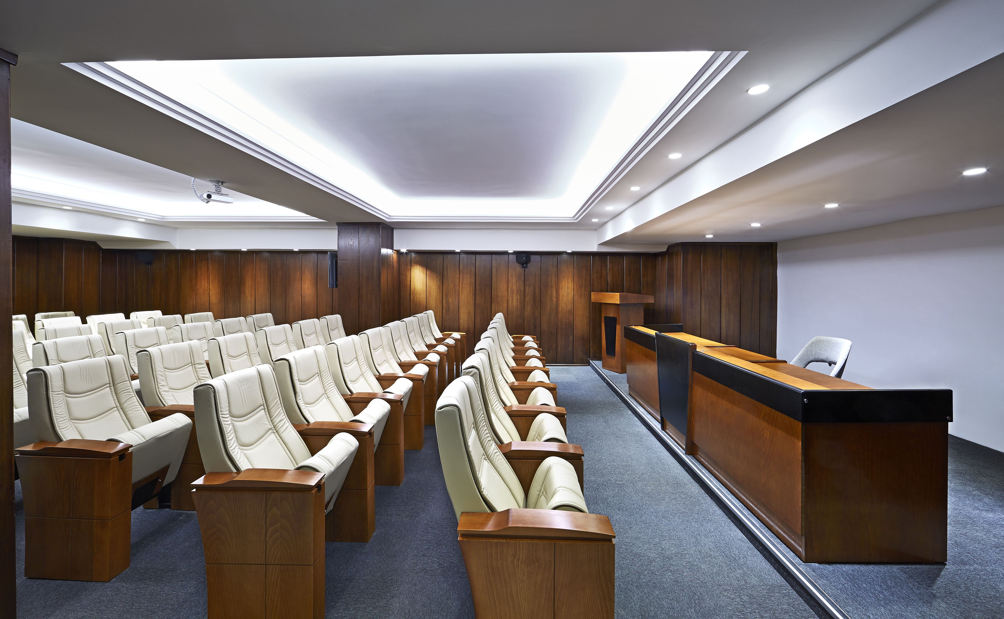 A conference room with rows of leather chairs, a wooden podium, and a ceiling with recessed lighting.