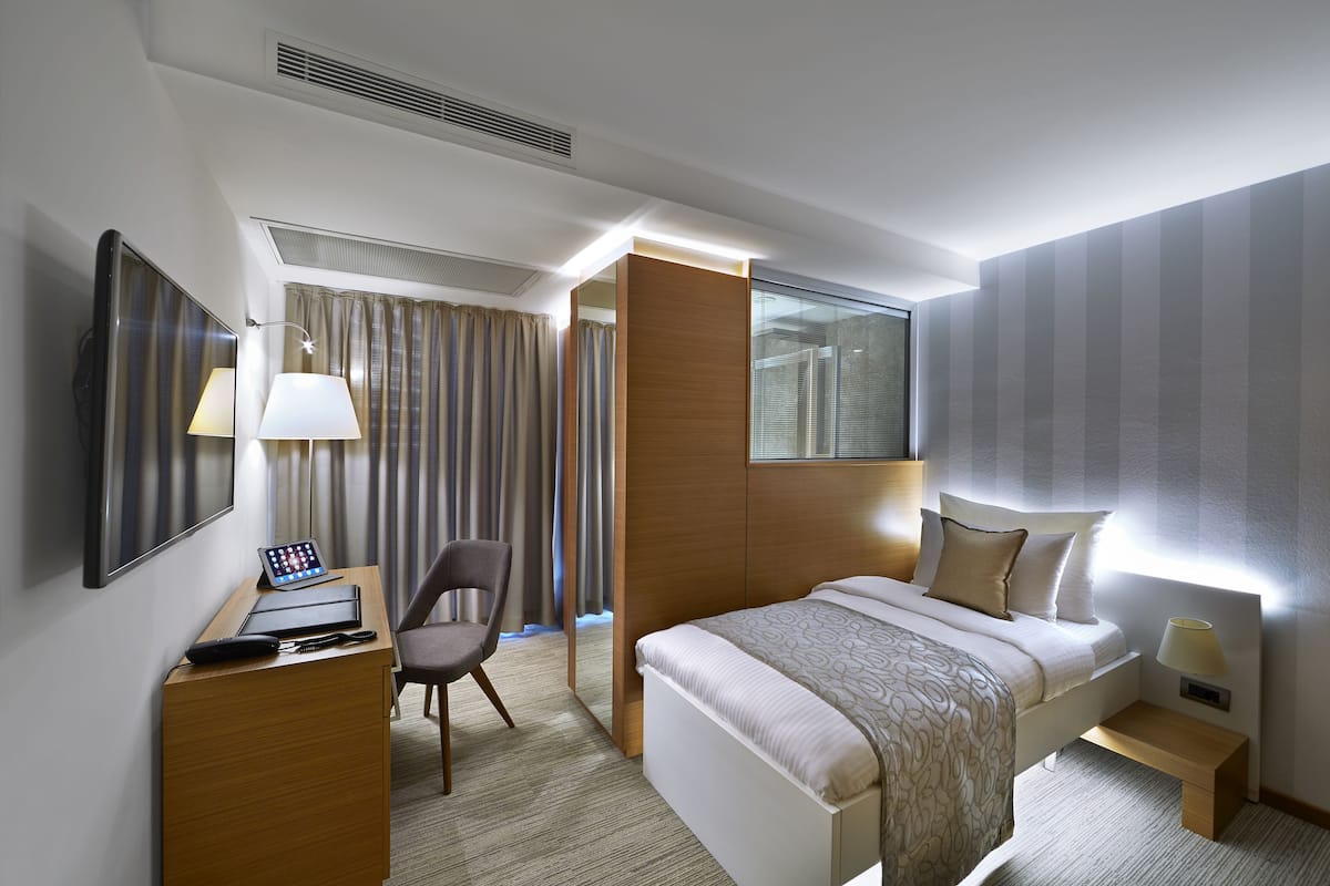 A hotel room with a bed, desk, chair, and a large mirror.