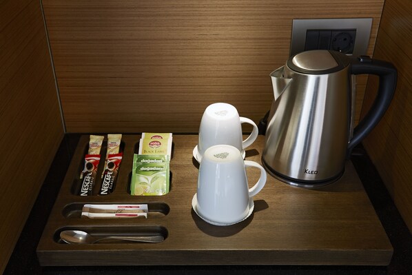 A coffee station with a kettle, cups, and coffee packets.