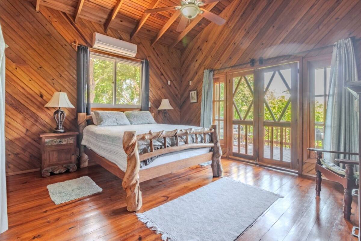 A wooden cabin bedroom with a bed, two nightstands, a ceiling fan, and large windows.