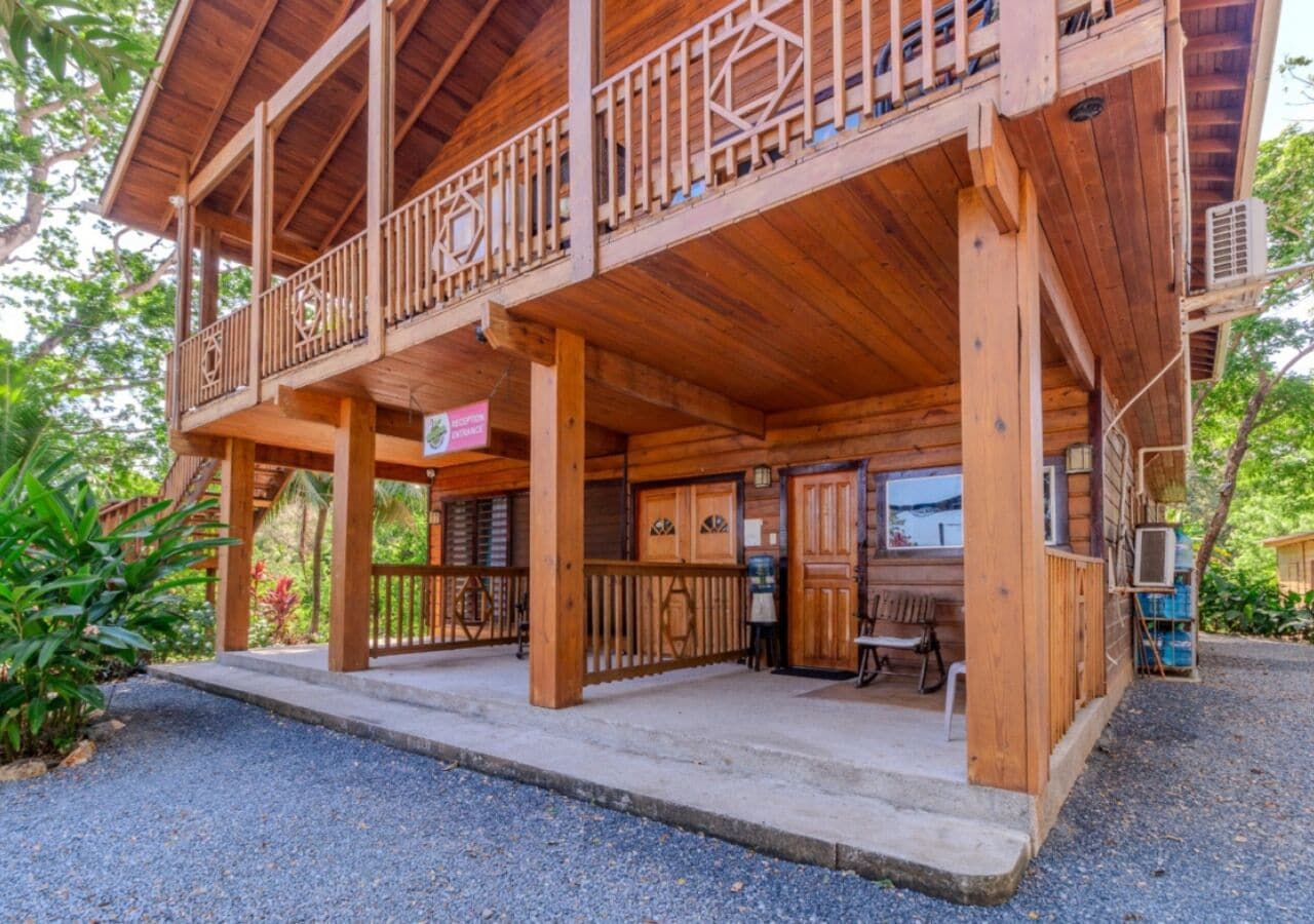 A wooden cabin with a balcony, a covered porch, and a small outdoor seating area.