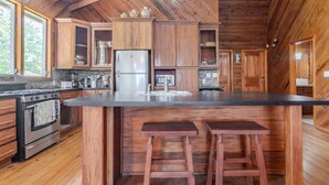 Une cuisine avec des meubles de rangement en bois, un grand îlot central doté de tabourets, un réfrigérateur et une cuisinière.