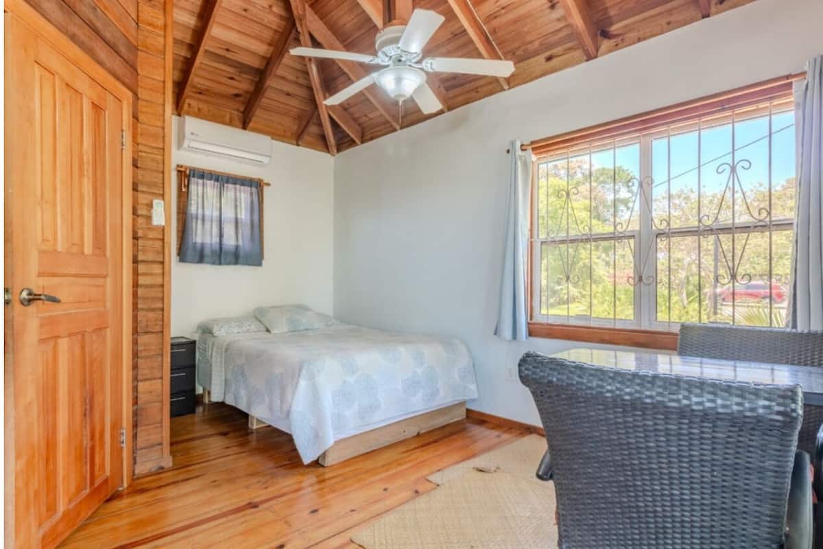 A bedroom with a bed, a ceiling fan, a window with curtains, and a wicker chair.