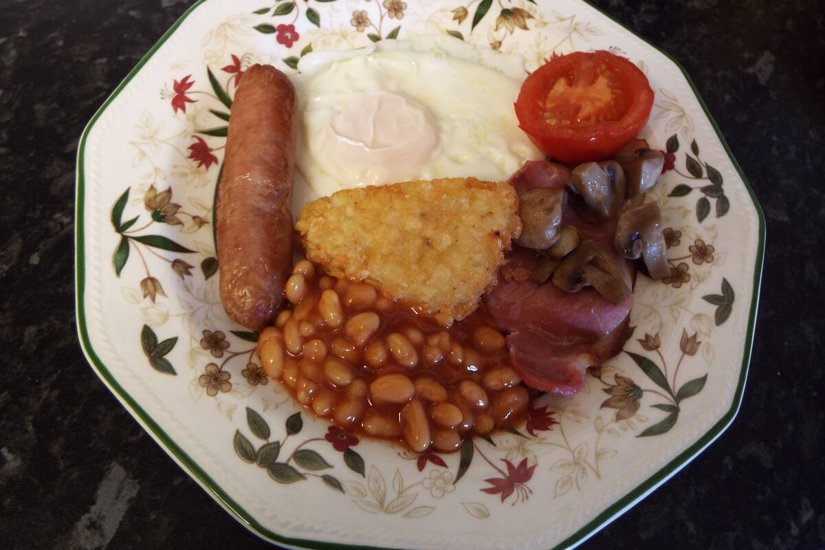 A plate with a variety of foods including sausages, eggs, beans, mushrooms, and a slice of tomato.