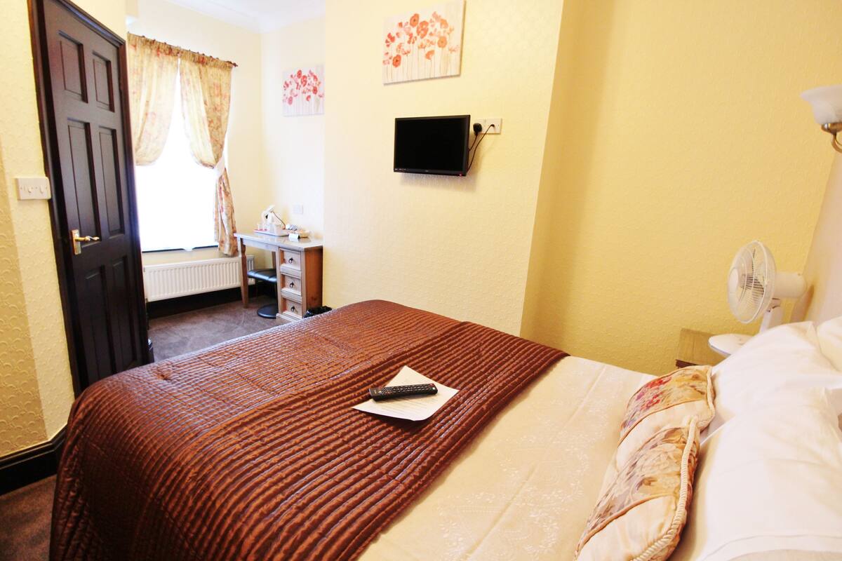 A hotel room with a bed, a desk, a television, and a window with curtains.