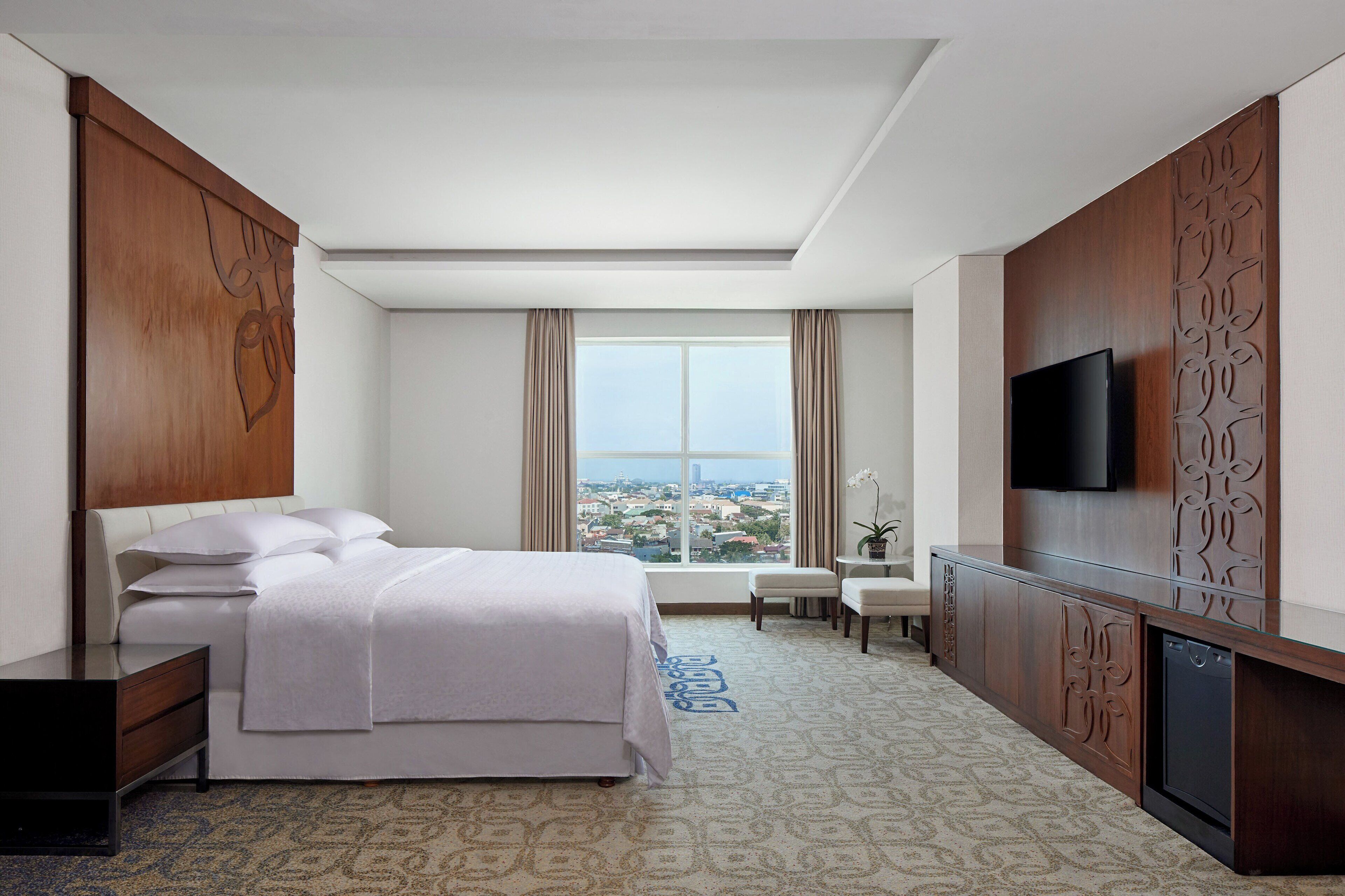 A hotel room with a bed, a desk, a television, and a window with a city view.