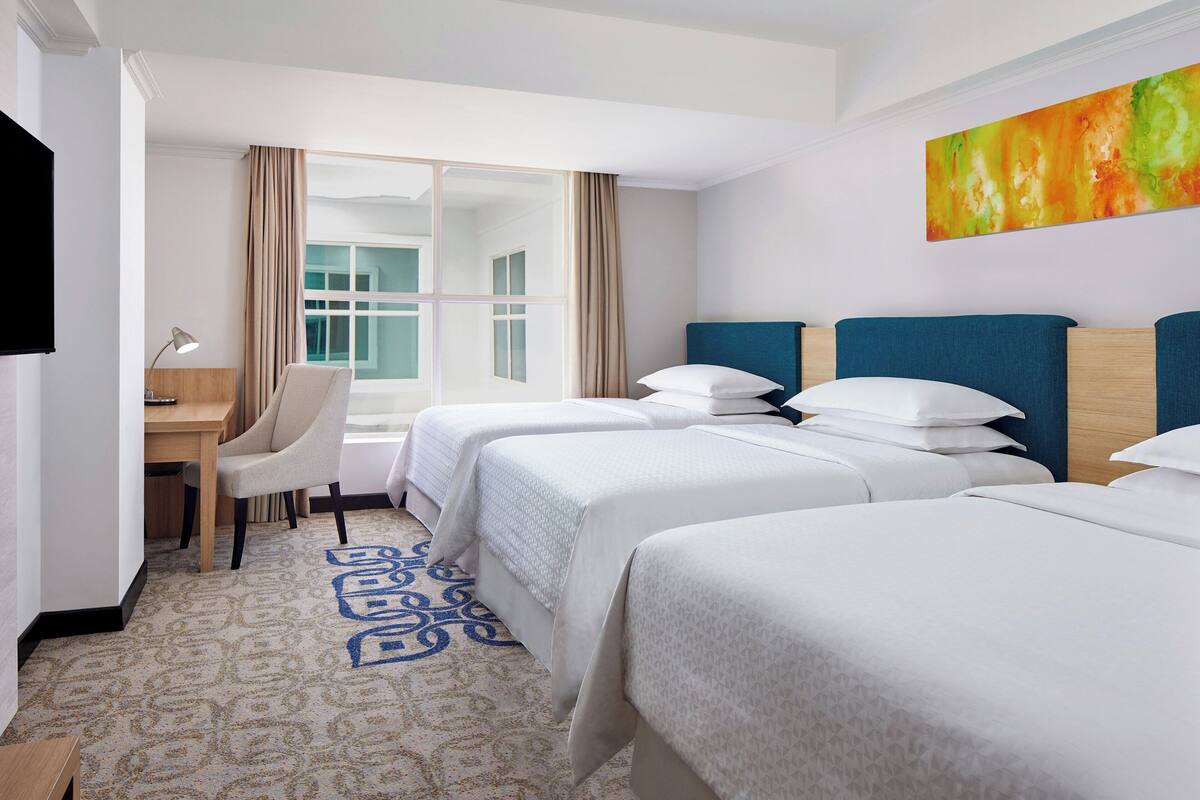 Une chambre d’hôtel avec deux lits, un bureau, une chaise, une télévision et une grande fenêtre avec des rideaux.
