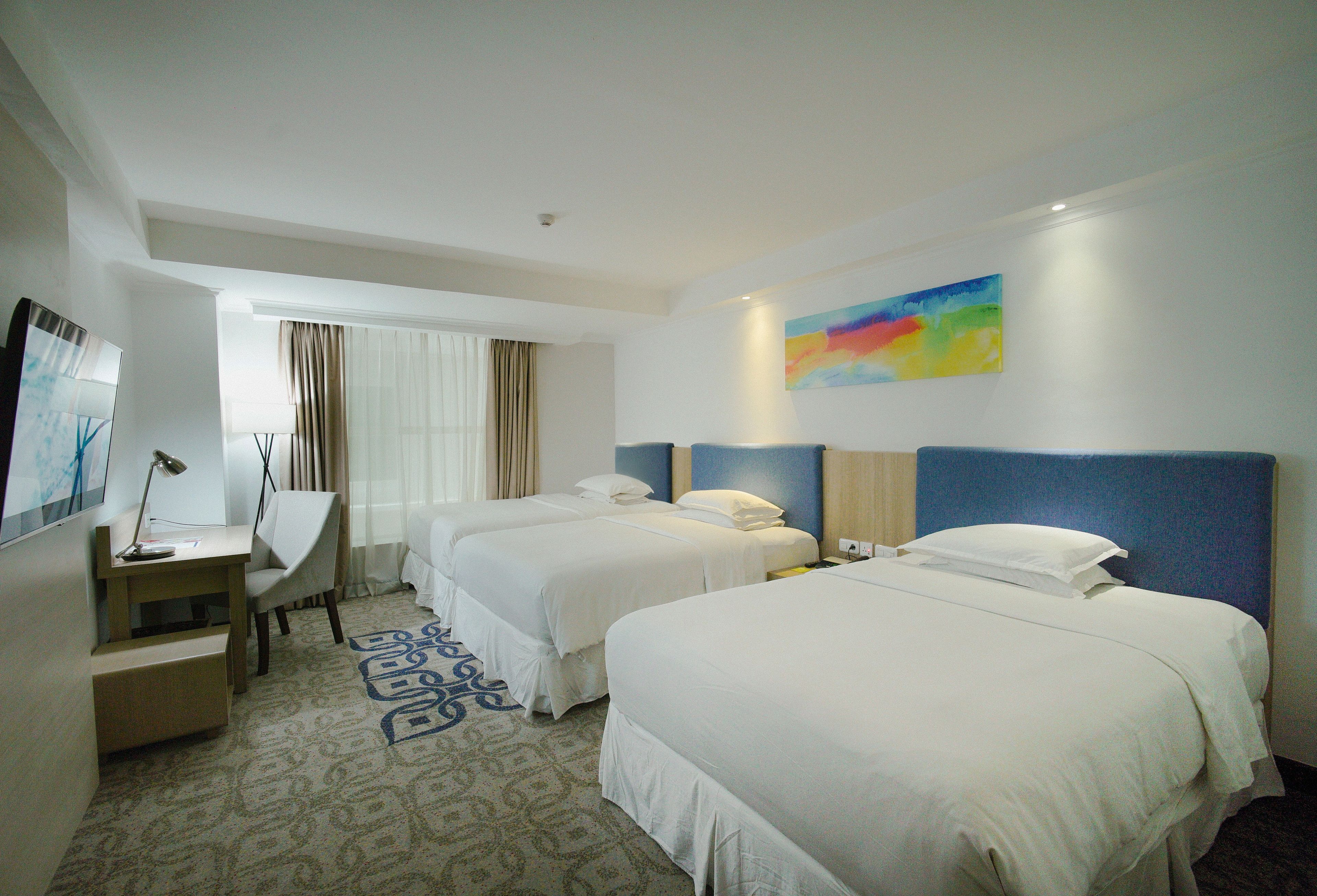 A hotel room with two beds, a desk, a chair, and a painting on the wall.