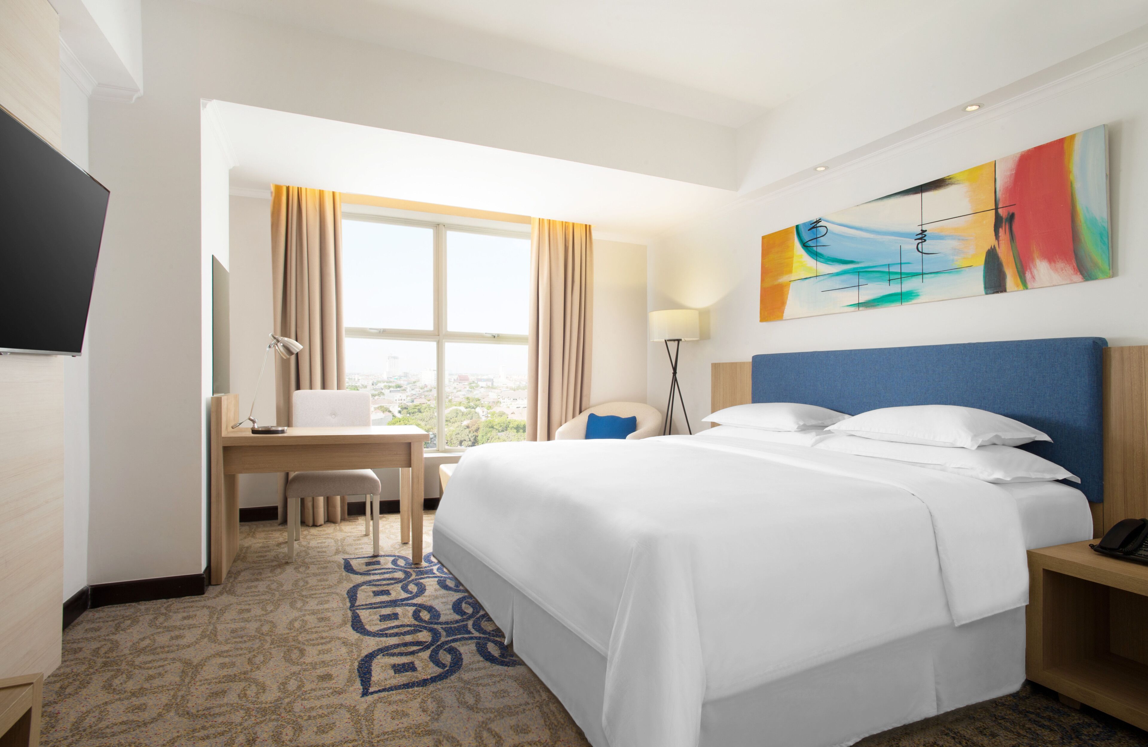 Une chambre d’hôtel avec un grand lit, un bureau avec un ordinateur portable, une télévision et une vue sur la ville.