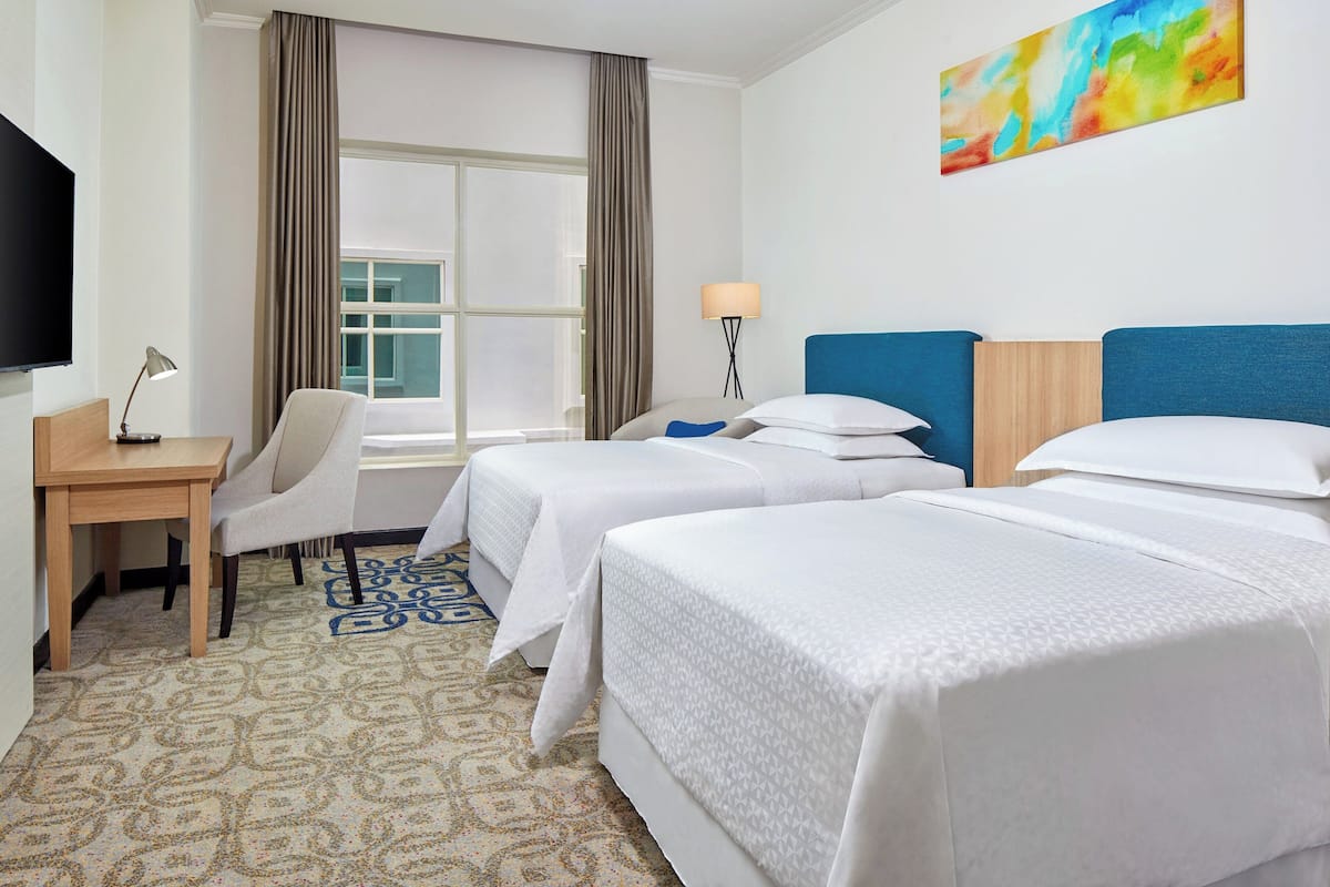 Une chambre d’hôtel avec deux lits, un bureau, une chaise, une télévision et une fenêtre avec des rideaux.