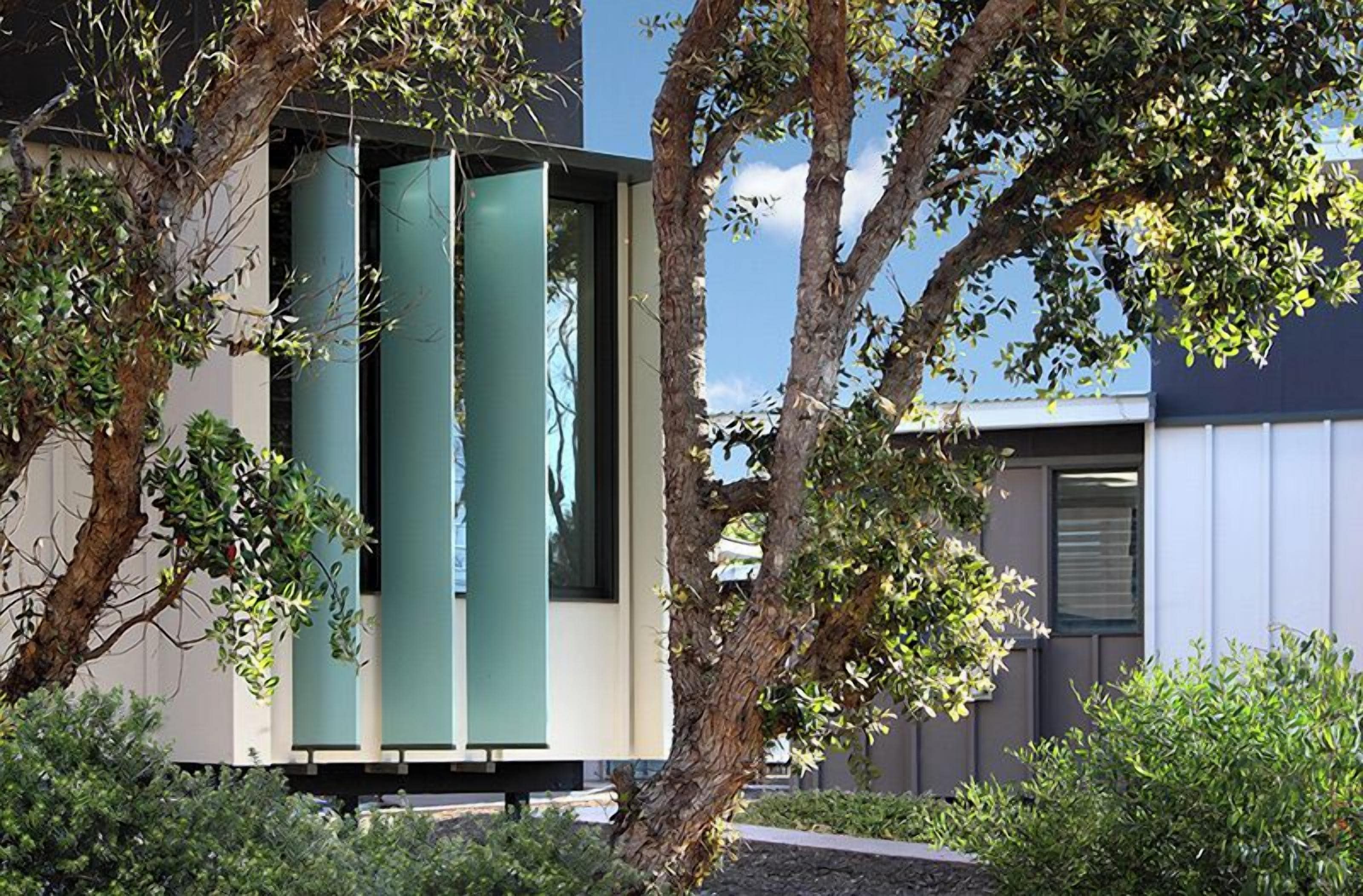 A modern building with large windows and a minimalist design, surrounded by trees and greenery.