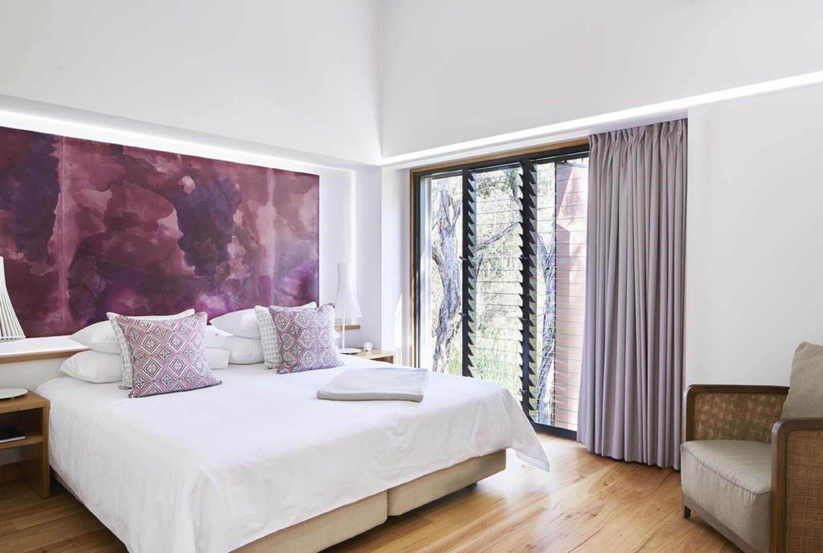 Un dormitorio moderno con una cama grande, una mesita de noche, una silla y un cuadro abstracto de gran tamaño en la pared.