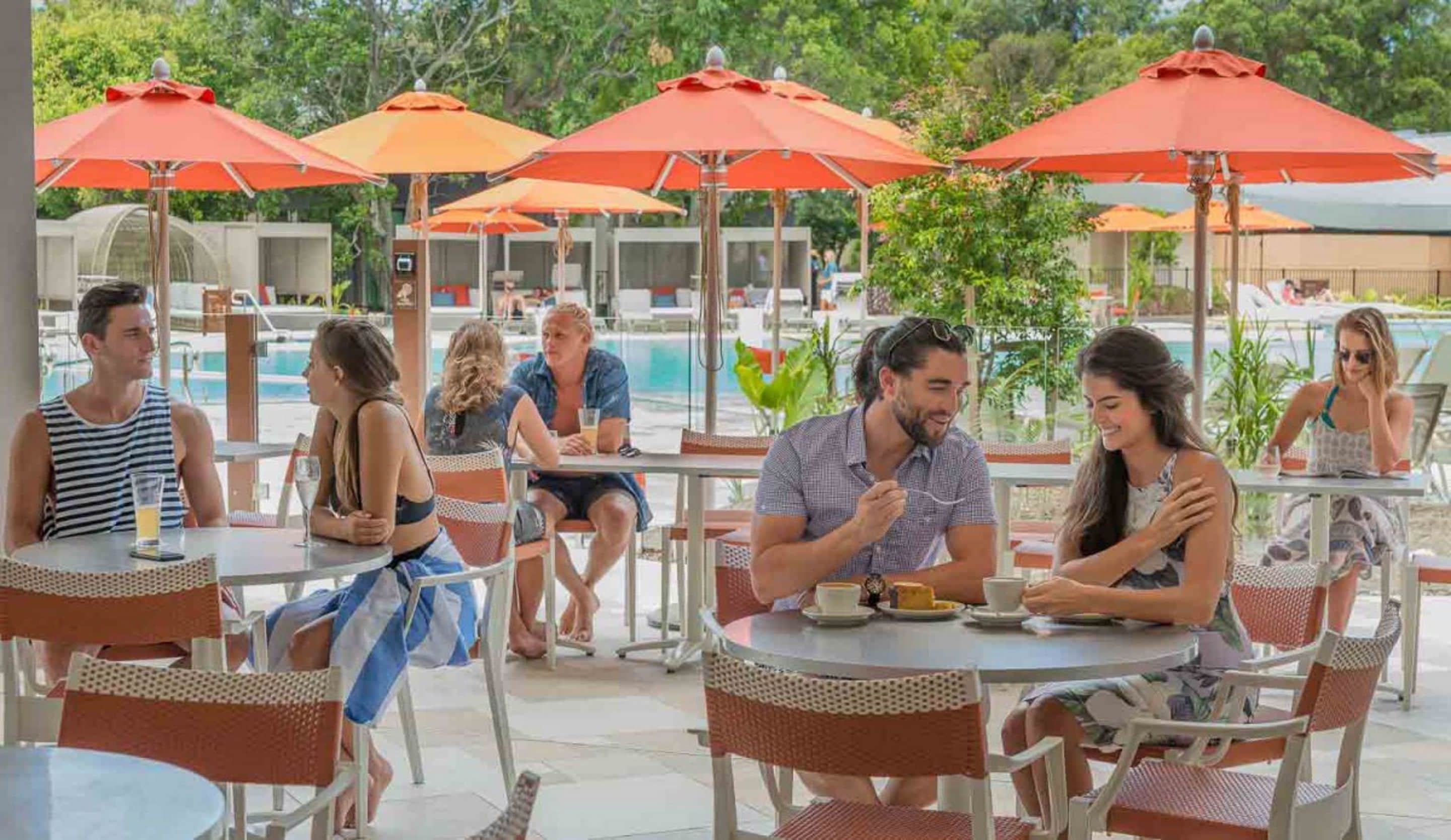 Un área de comedor junto a la piscina con mesas exteriores y sombrillas anaranjadas.