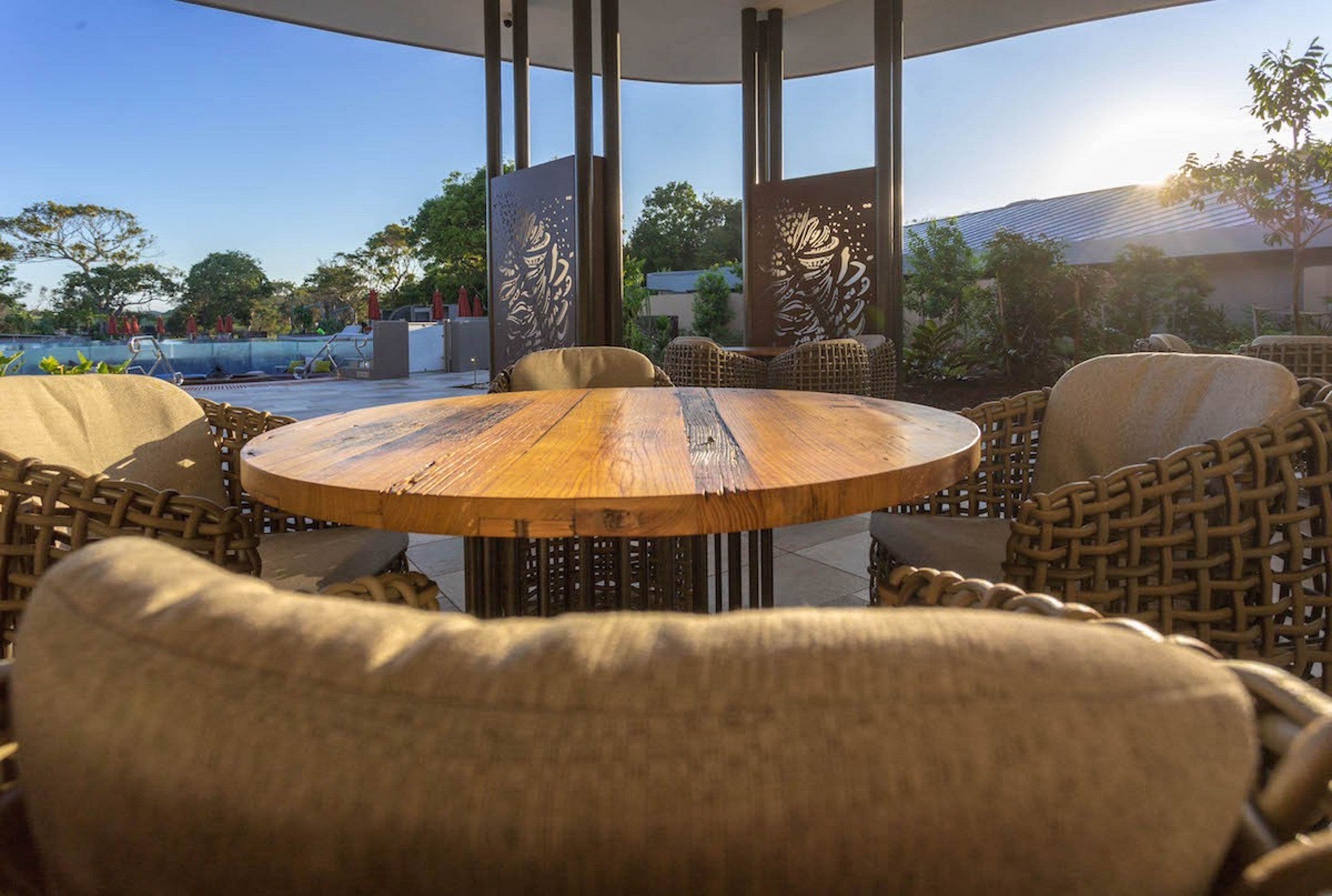 Un espacio al aire libre con una mesa redonda de madera y sillas de mimbre, rodeado de paneles decorativos con diseños elaborados.