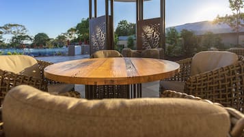 An outdoor seating area with a round wooden table and wicker chairs, surrounded by decorative panels with intricate designs.