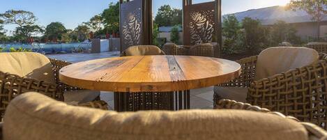 Un espacio al aire libre con una mesa redonda de madera y sillas de mimbre, rodeado de paneles decorativos con diseños elaborados.