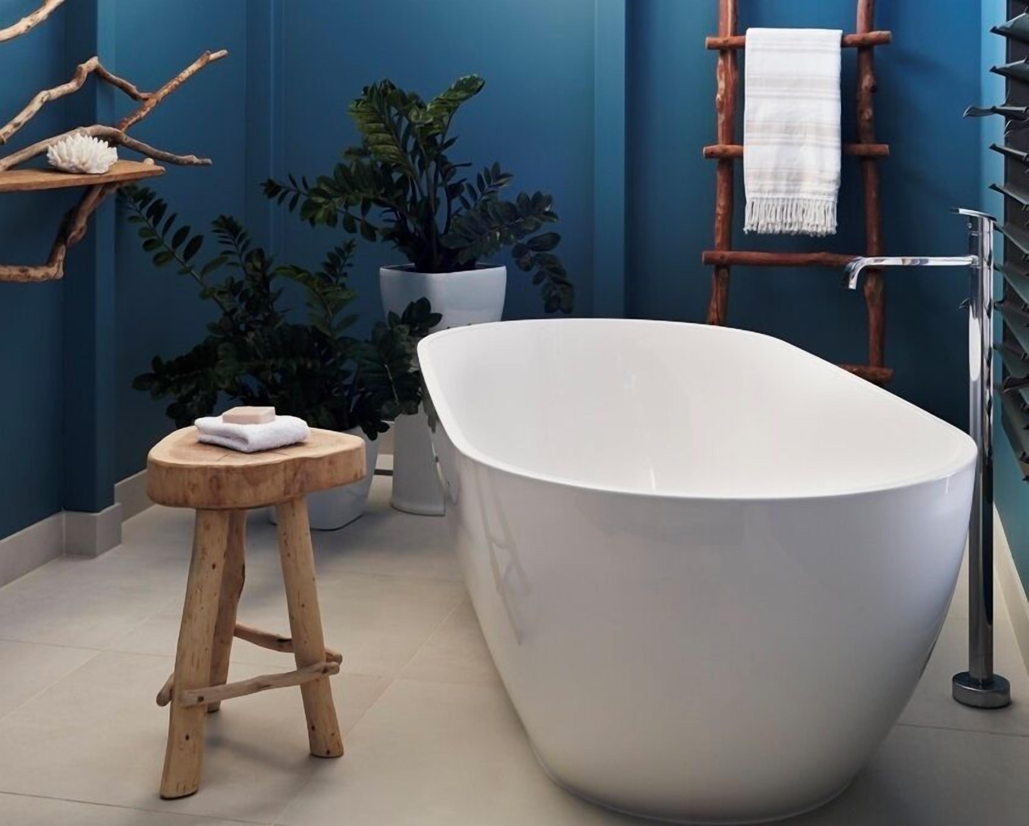 A modern bathroom with a freestanding bathtub, a wooden stool, a potted plant, and a towel rack.