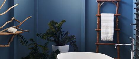 A modern bathroom with a freestanding bathtub, wooden stool, potted plants, and a towel rack.
