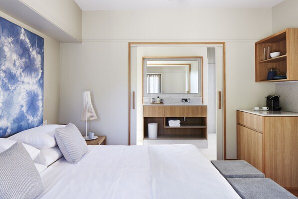 Una habitación de hotel moderna con una cama grande, un baño con espejo y una kitchenette.