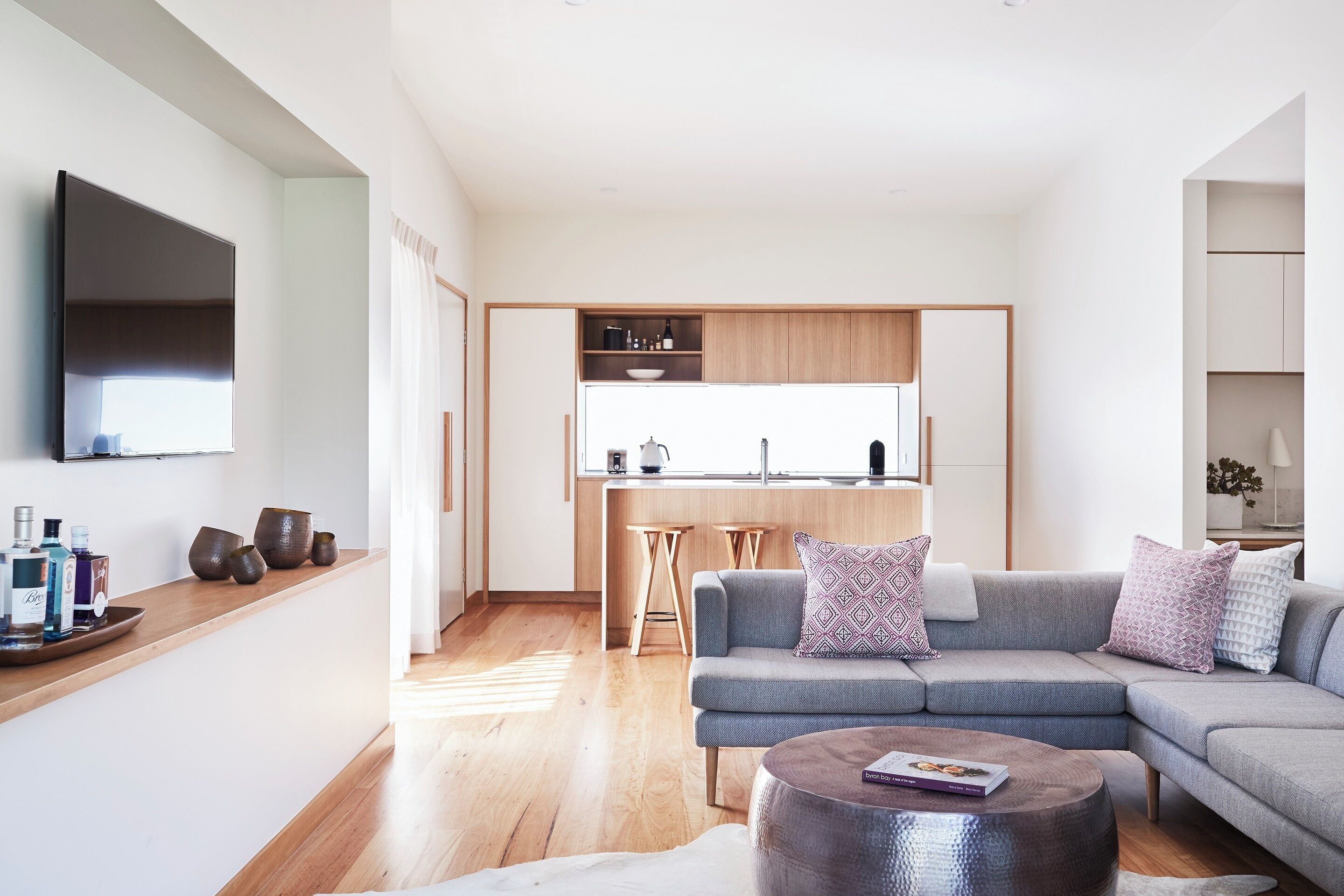A modern living room with a grey sectional sofa, a coffee table, and a kitchen area in the background.