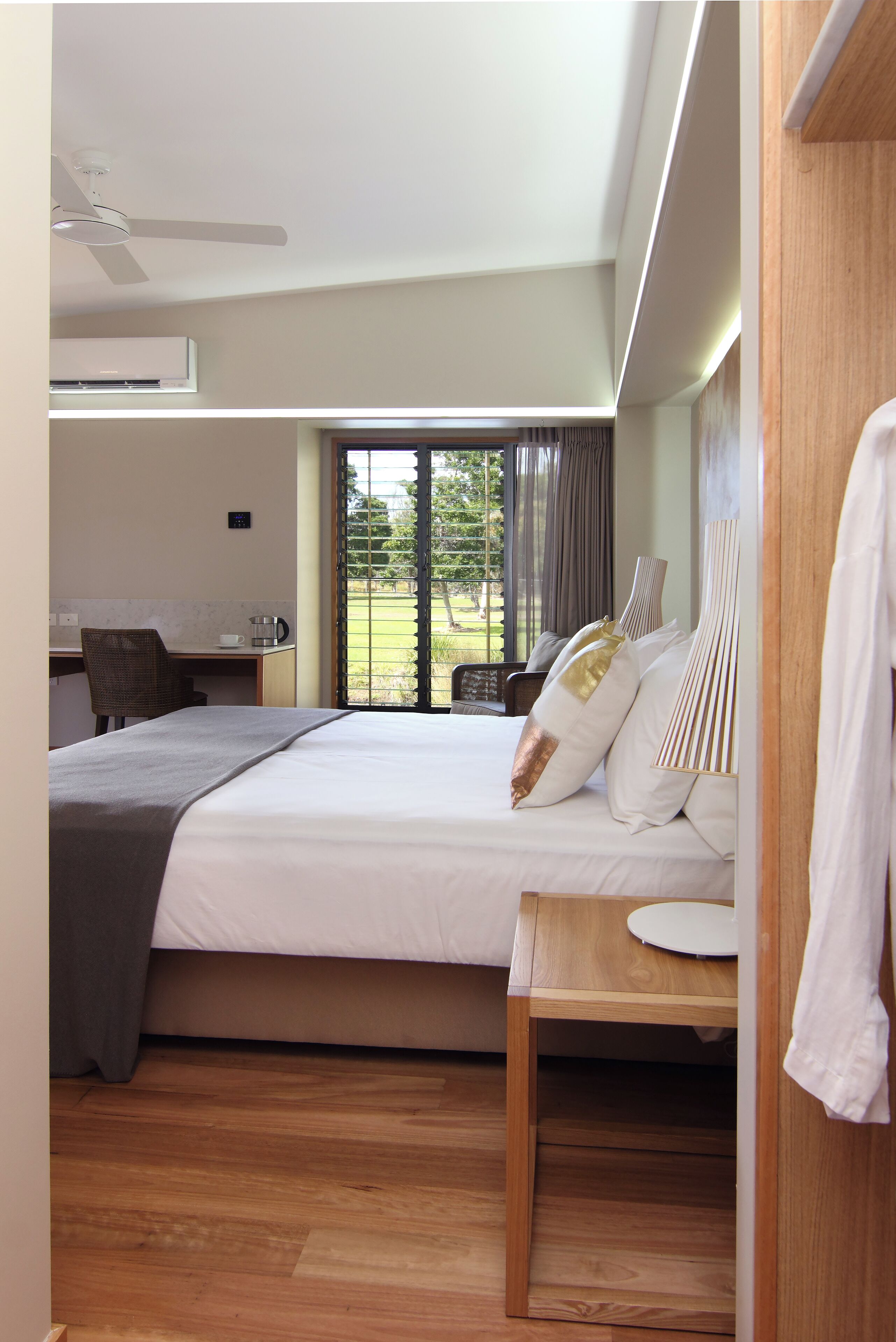 A modern hotel room with a large bed, a desk, and a view of the outdoors.