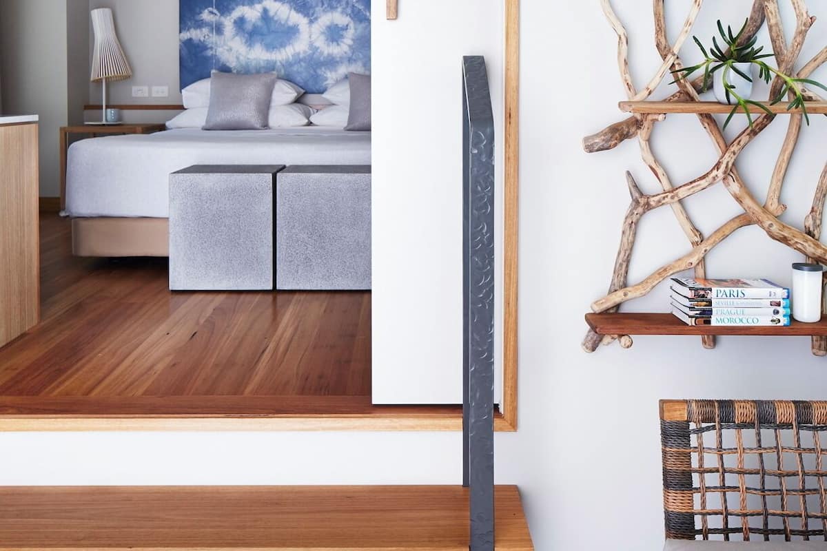 A modern bedroom with a bed, bedside table, and a wall-mounted shelf with books and a plant.