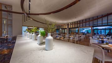 A spacious indoor dining area with a long marble counter, white vases with plants, and a modern ceiling design.