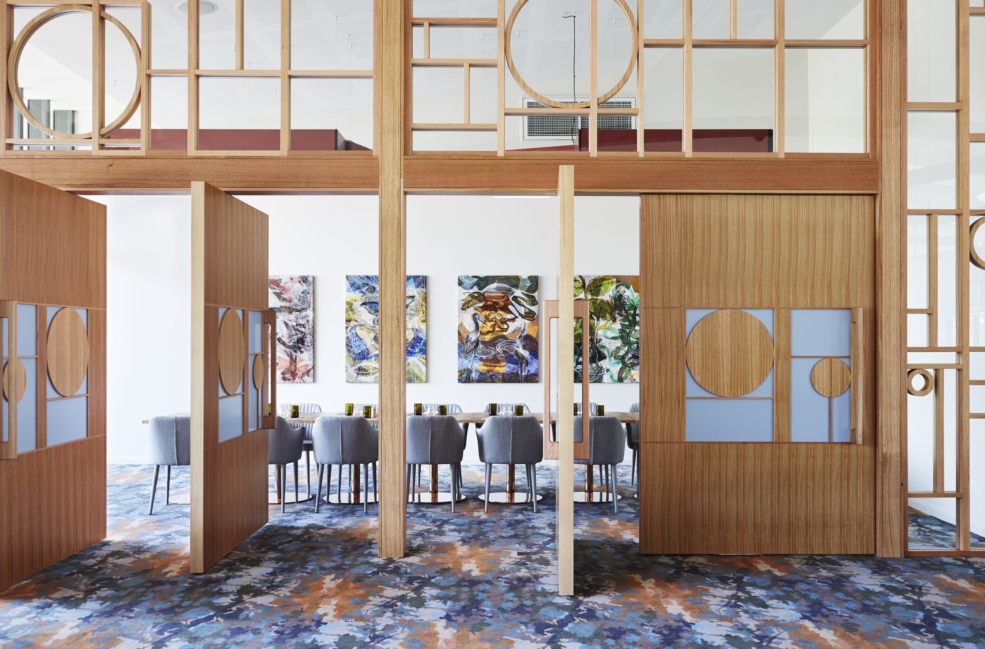 A modern dining area with wooden partitions, a blue floral carpet, and a view of the cityscape.
