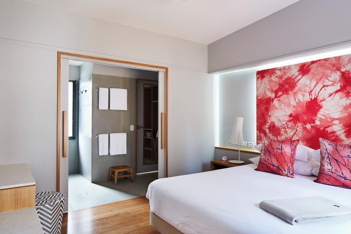 A modern hotel room with a large bed, a walk-in closet, and a bathroom with a shower and toilet.