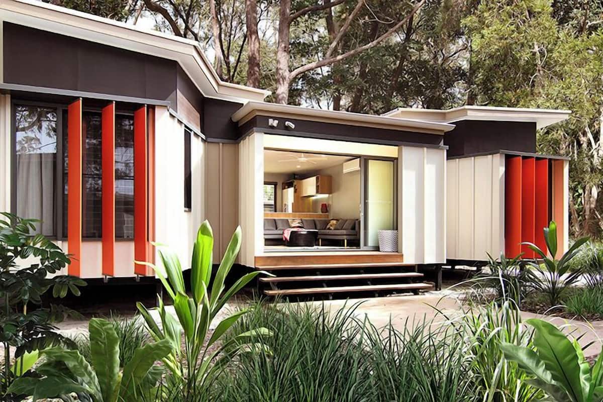 A modern house with a large glass door leading to a living area, surrounded by lush greenery.