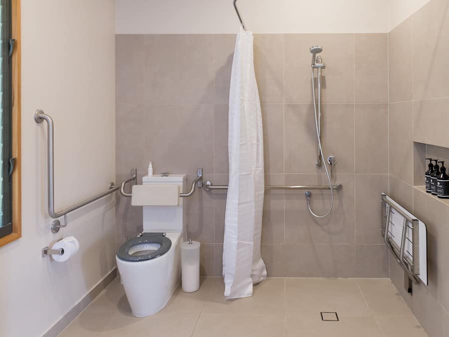 Een moderne badkamer met toilet, bidet, douche en handsteunen.
