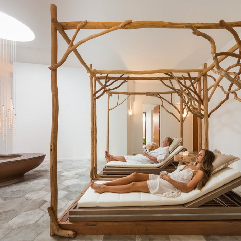 A room with a wooden canopy bed, a large mirror, and a stone-tiled floor.