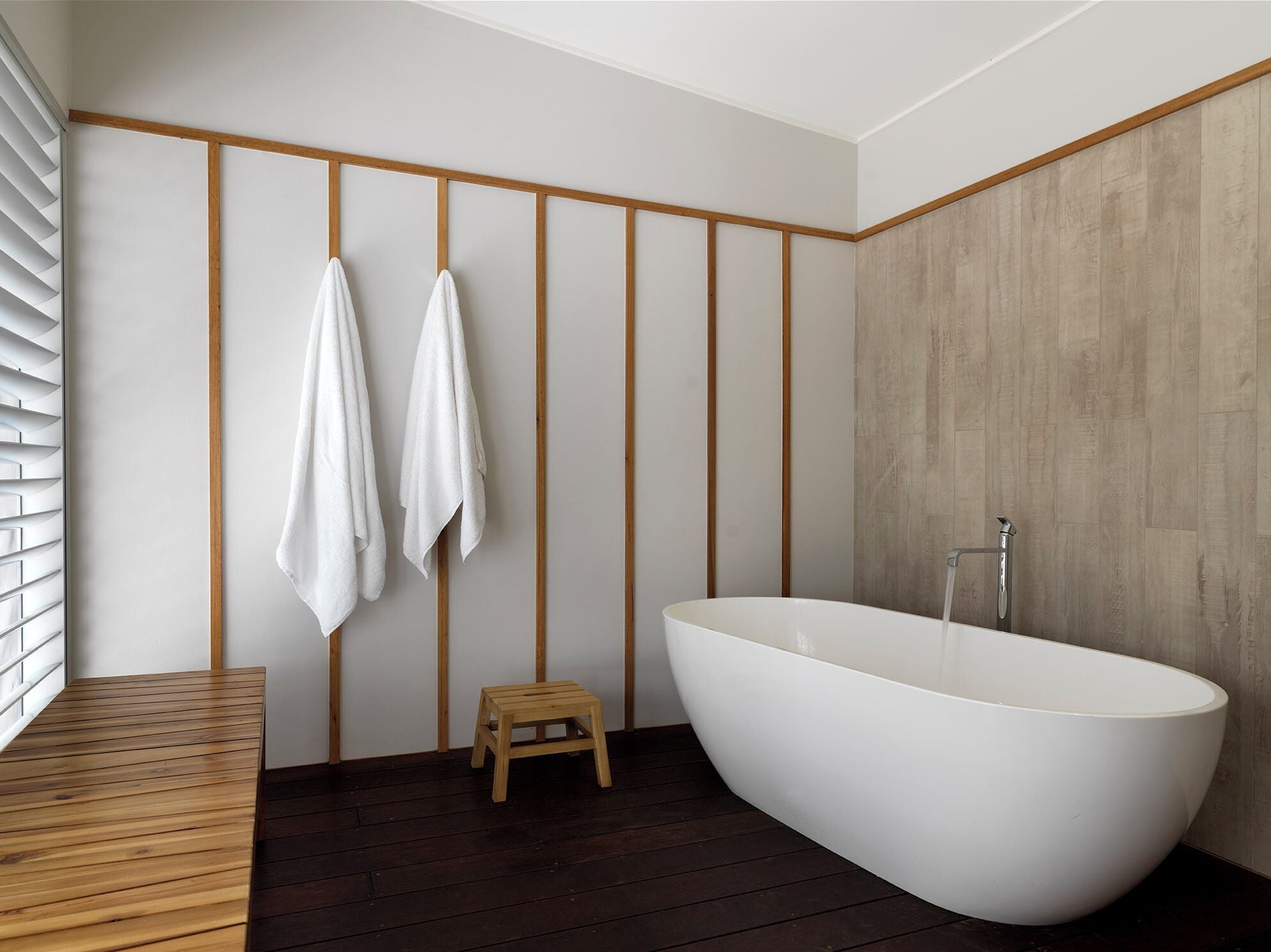 Une salle de bain moderne avec une baignoire sur pieds, un plancher en bois et un petit tabouret en bois.