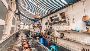 A bar area with a striped ceiling, bar stools, shelves with bottles, and a counter. - Casa Tuxi (Rio de Janeiro)