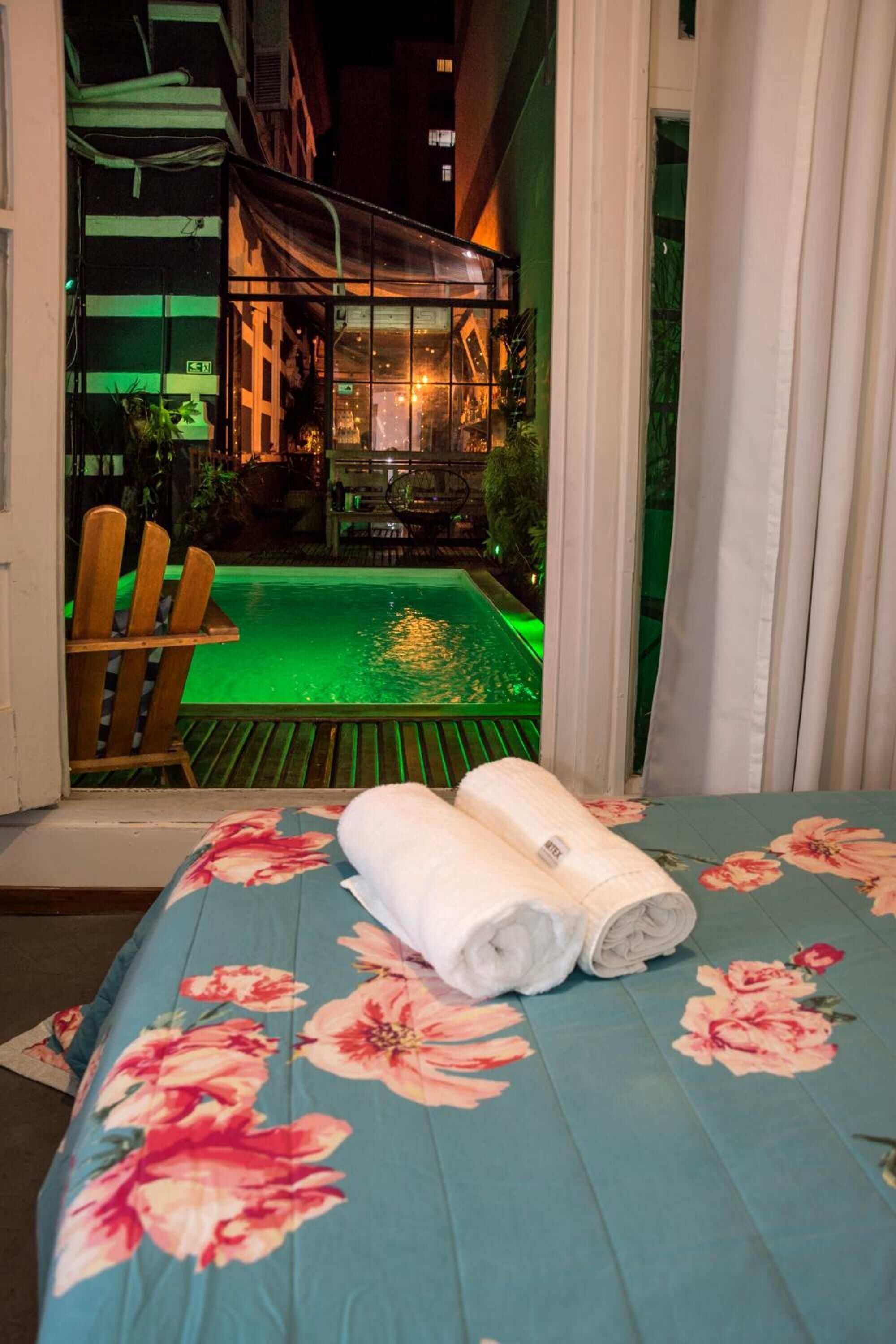 A hotel room with a bed, a view of an outdoor pool, and a chair by the pool.
