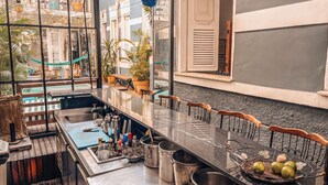 A kitchen with a long counter, stainless steel appliances, and a view of the street through large windows. - Casa Tuxi (Rio de Janeiro)