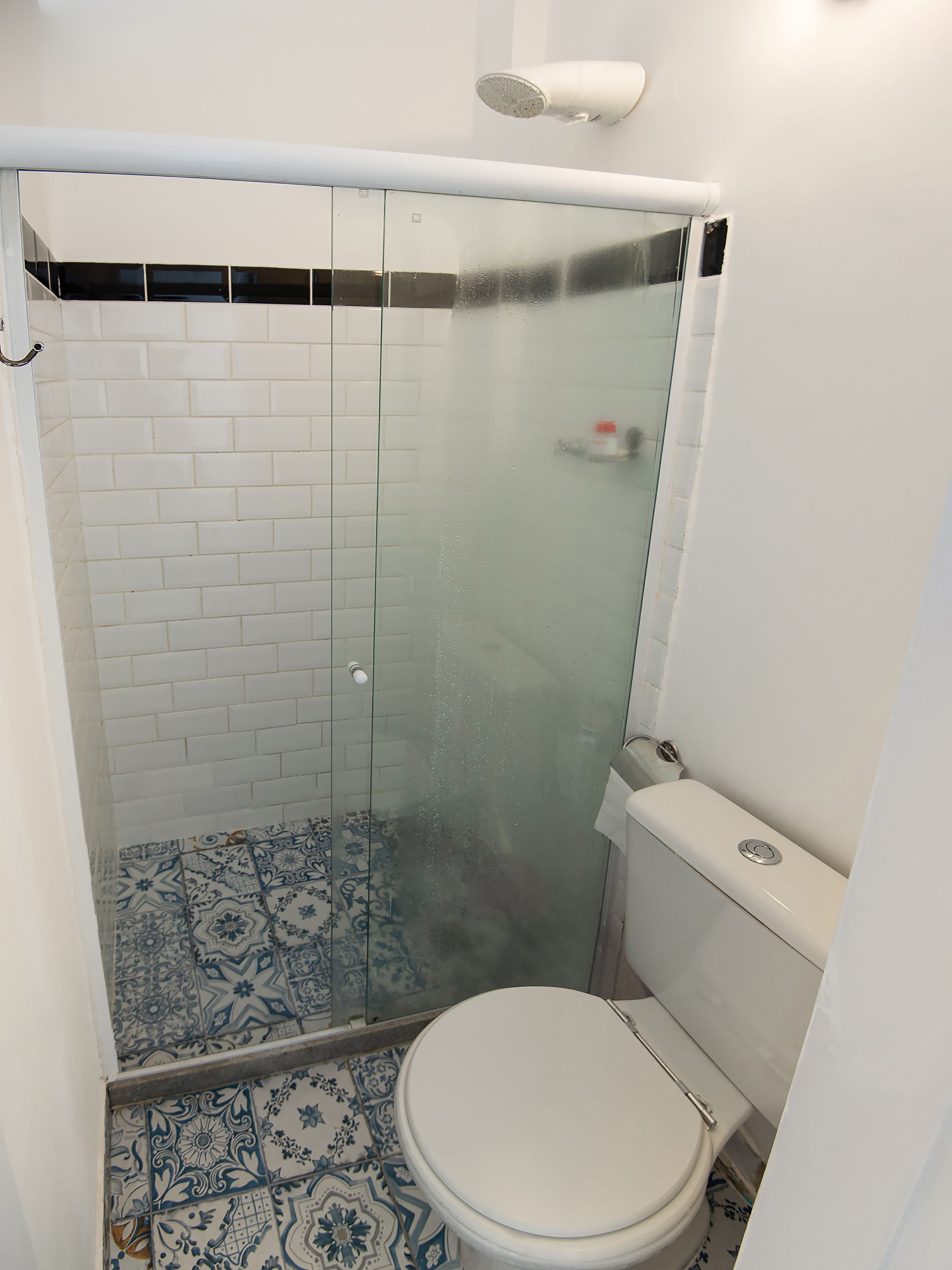 A bathroom with a glass-enclosed shower, a toilet, and patterned floor tiles.