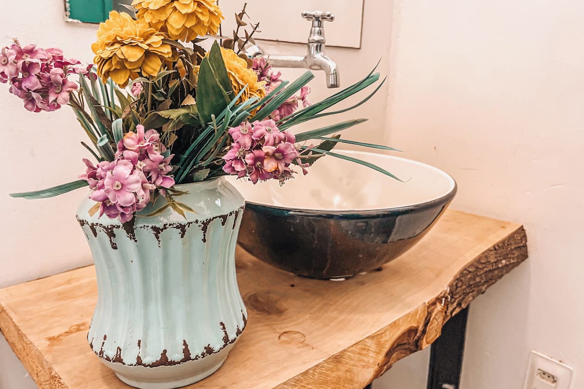 A bathroom with a wooden vanity, a white sink, and a vase with flowers.