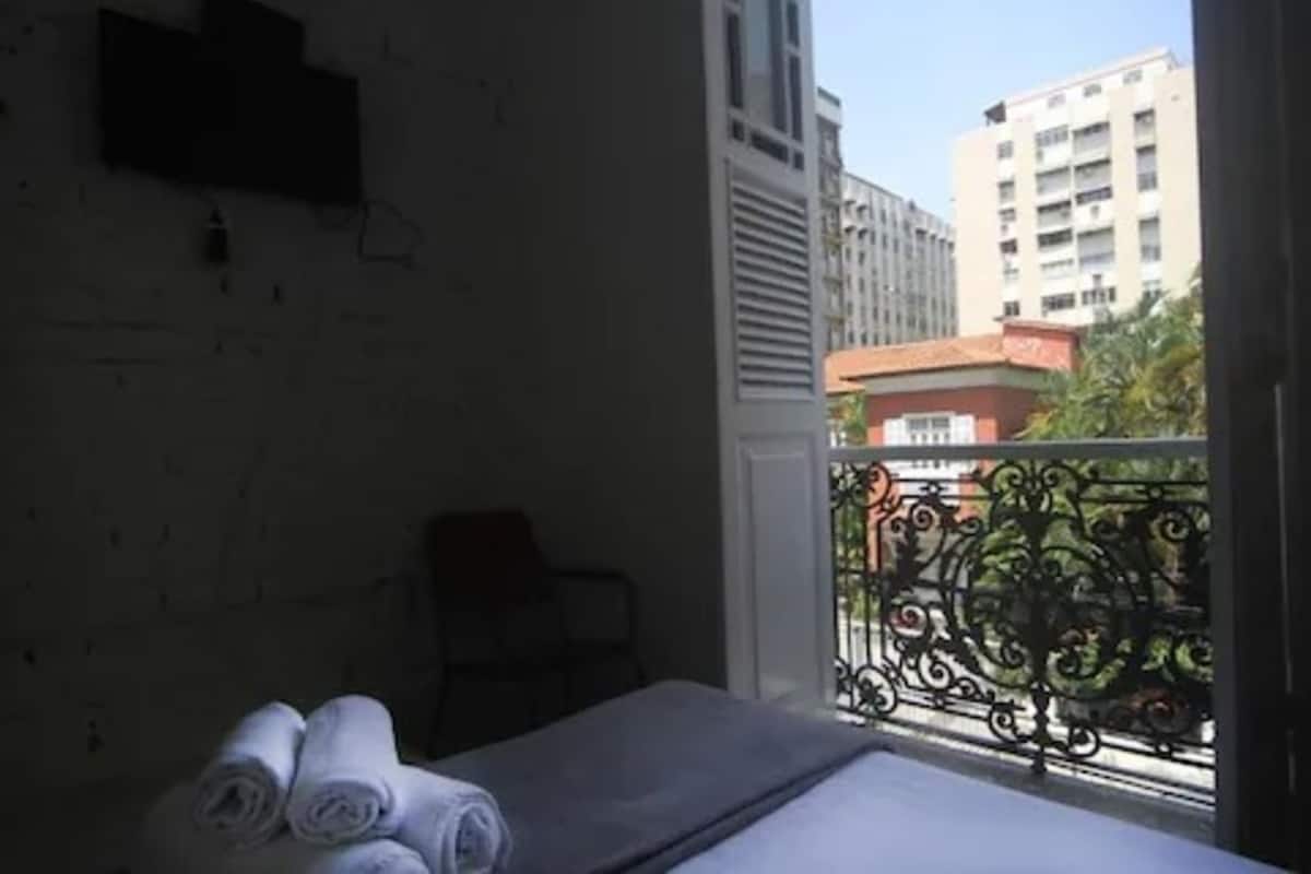 A hotel room with a bed, a chair, and a balcony with decorative railing.