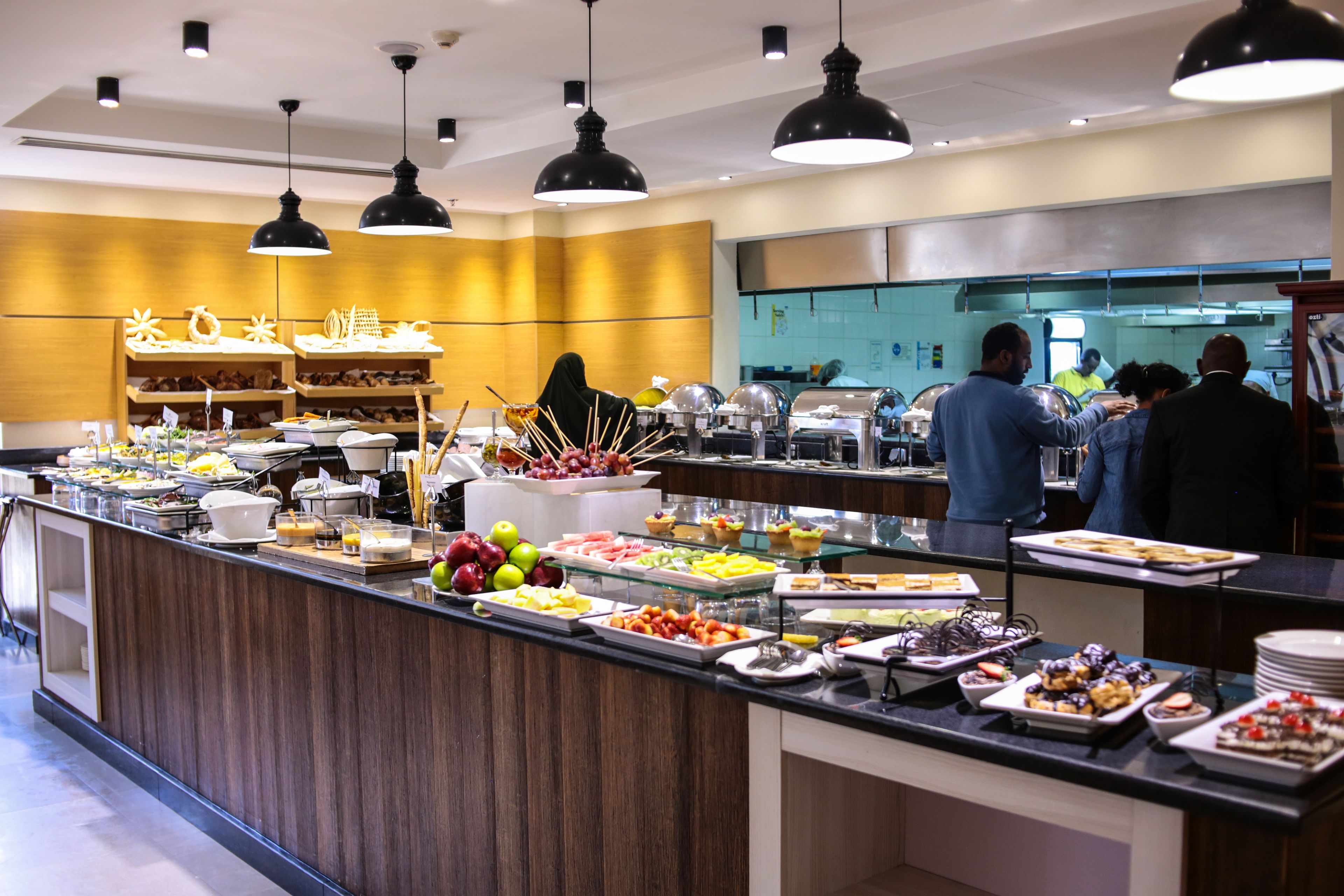 A buffet with various food items and a kitchen area in the background.