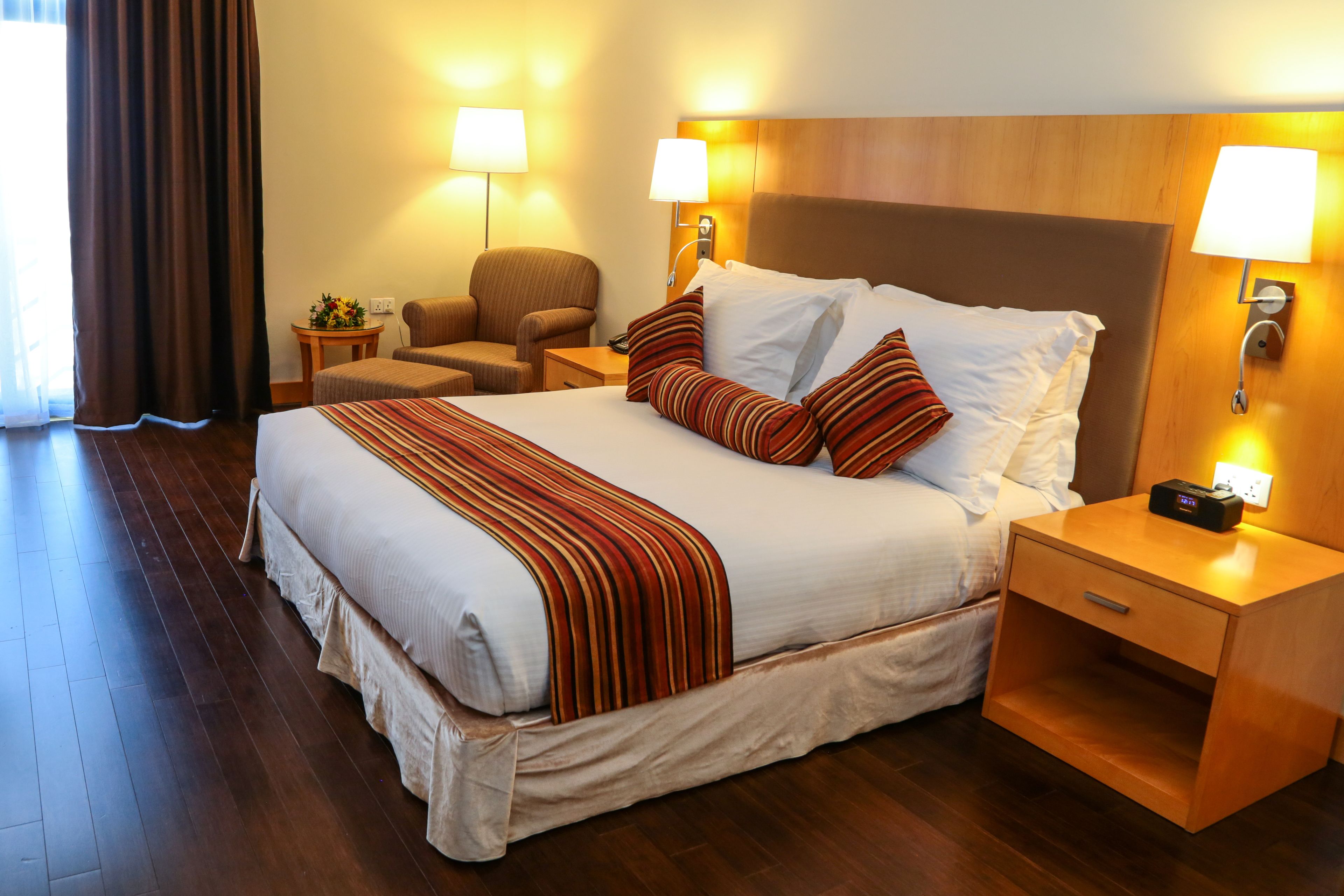 A hotel room with a large bed, two bedside tables, a chair, and a lamp.