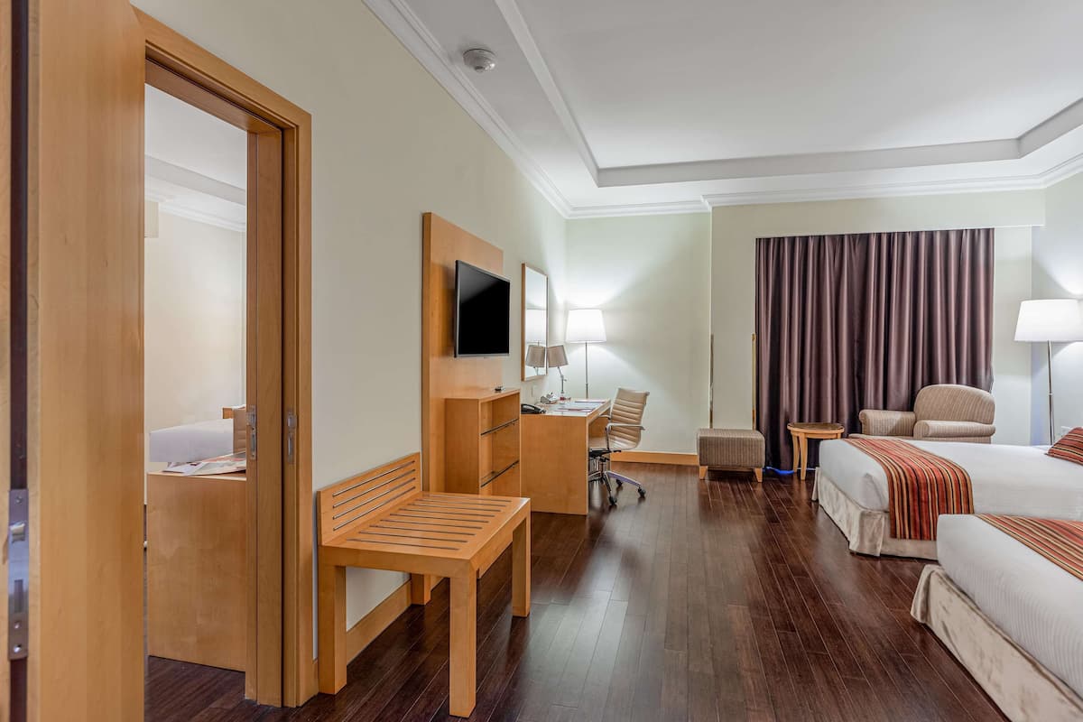 A hotel room with a wooden desk, a bed, a chair, a TV, and a window with curtains.