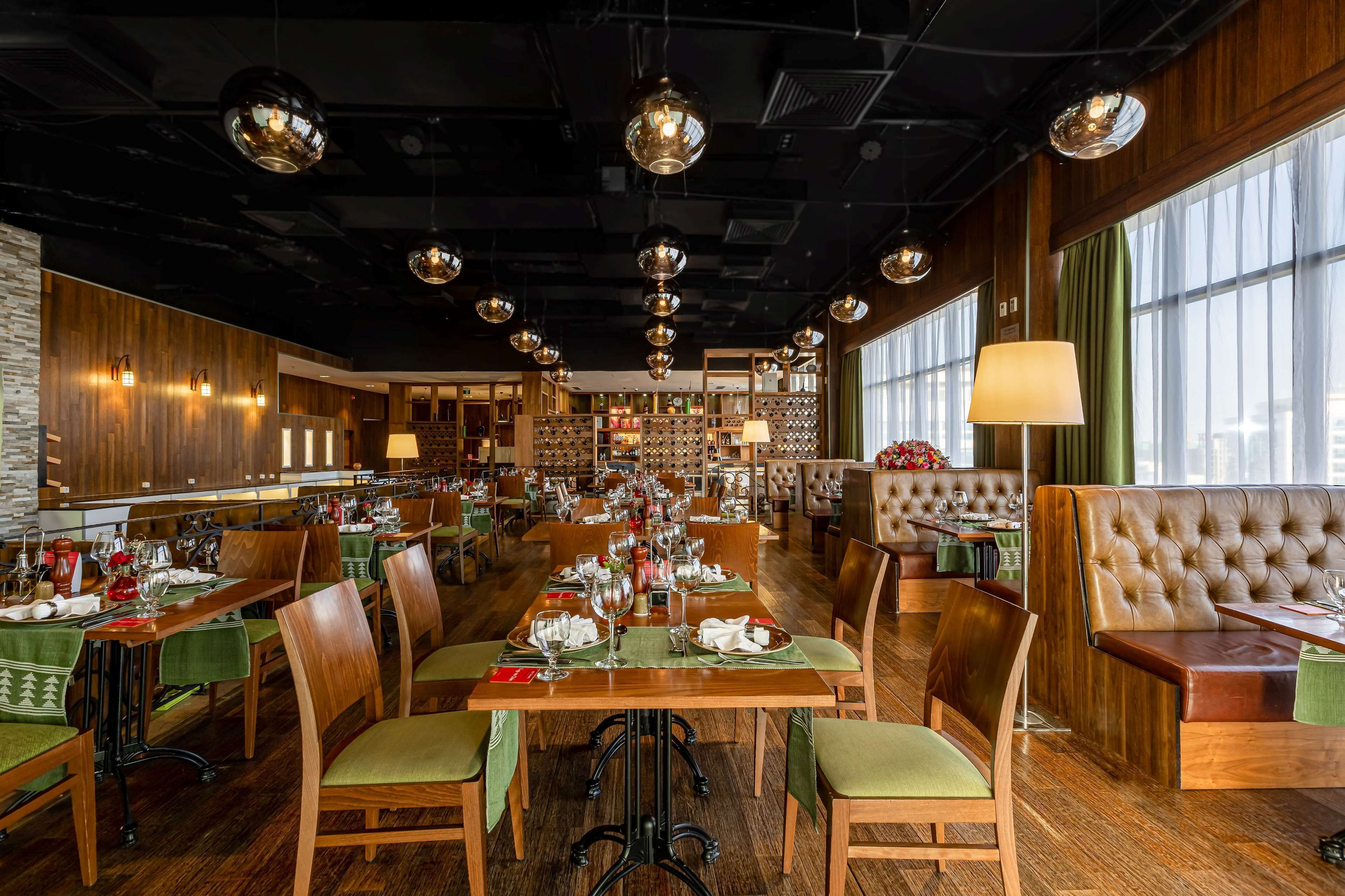 A restaurant with wooden tables and chairs, a bar area, and a seating section with a green curtain.