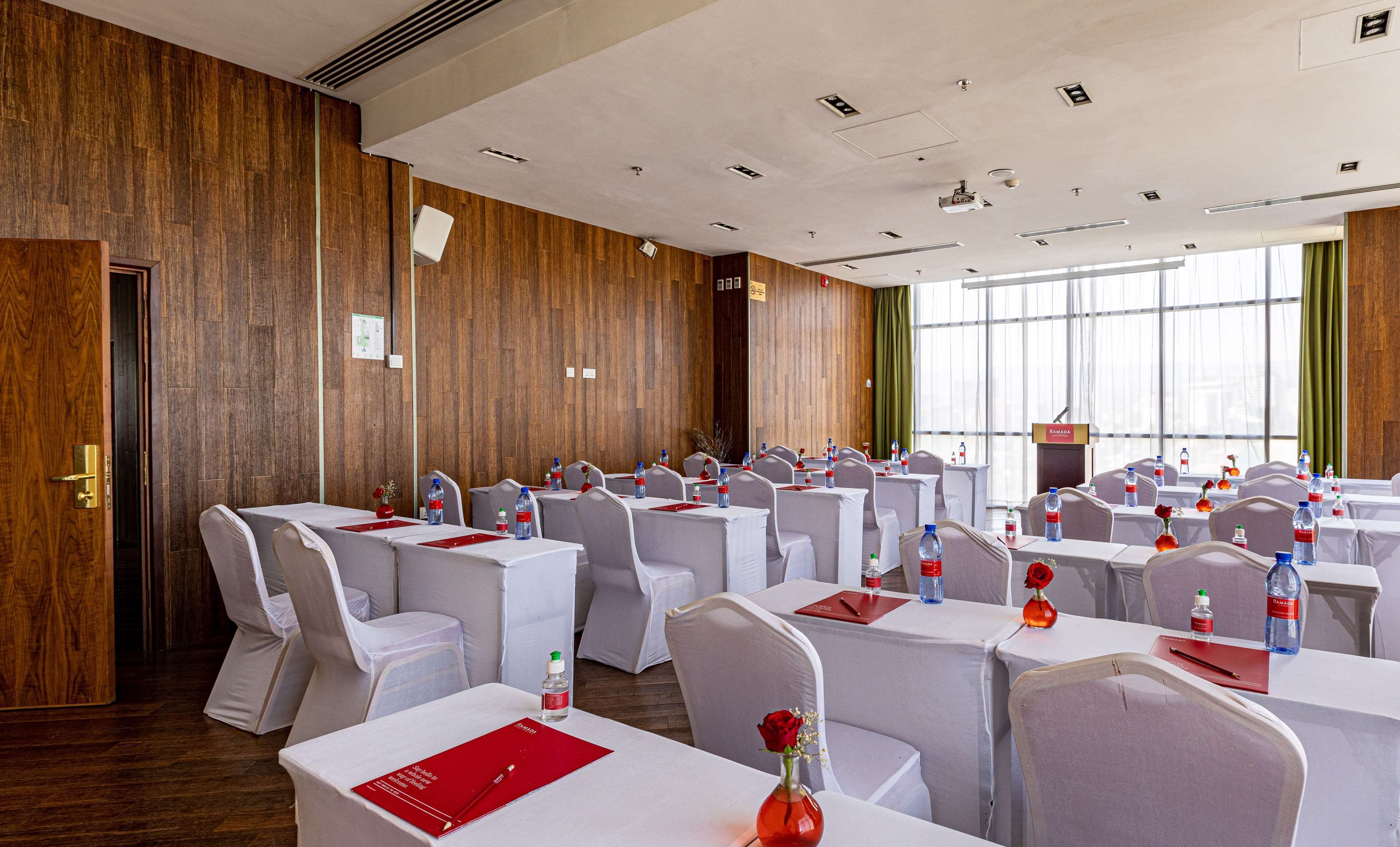 A conference room with rows of tables and chairs, a podium, and a large window.